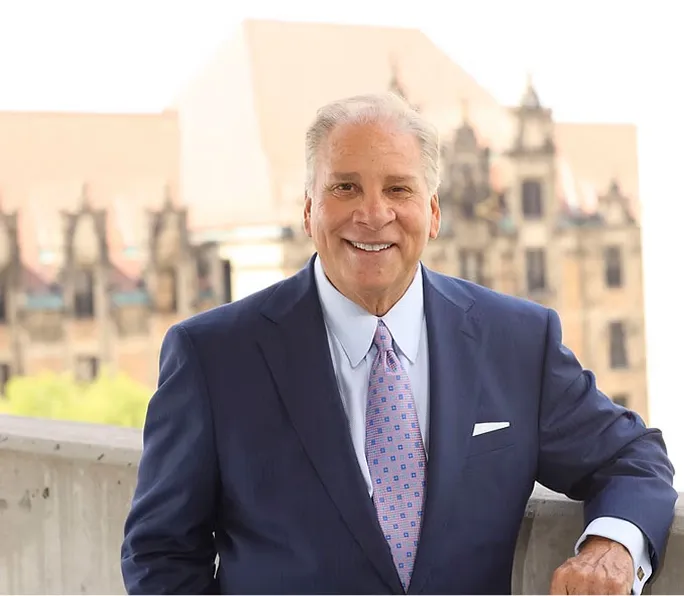 Portrait of Collector of Revenue Gregory F.X. Daly in a suit, standing in front of a historic building.